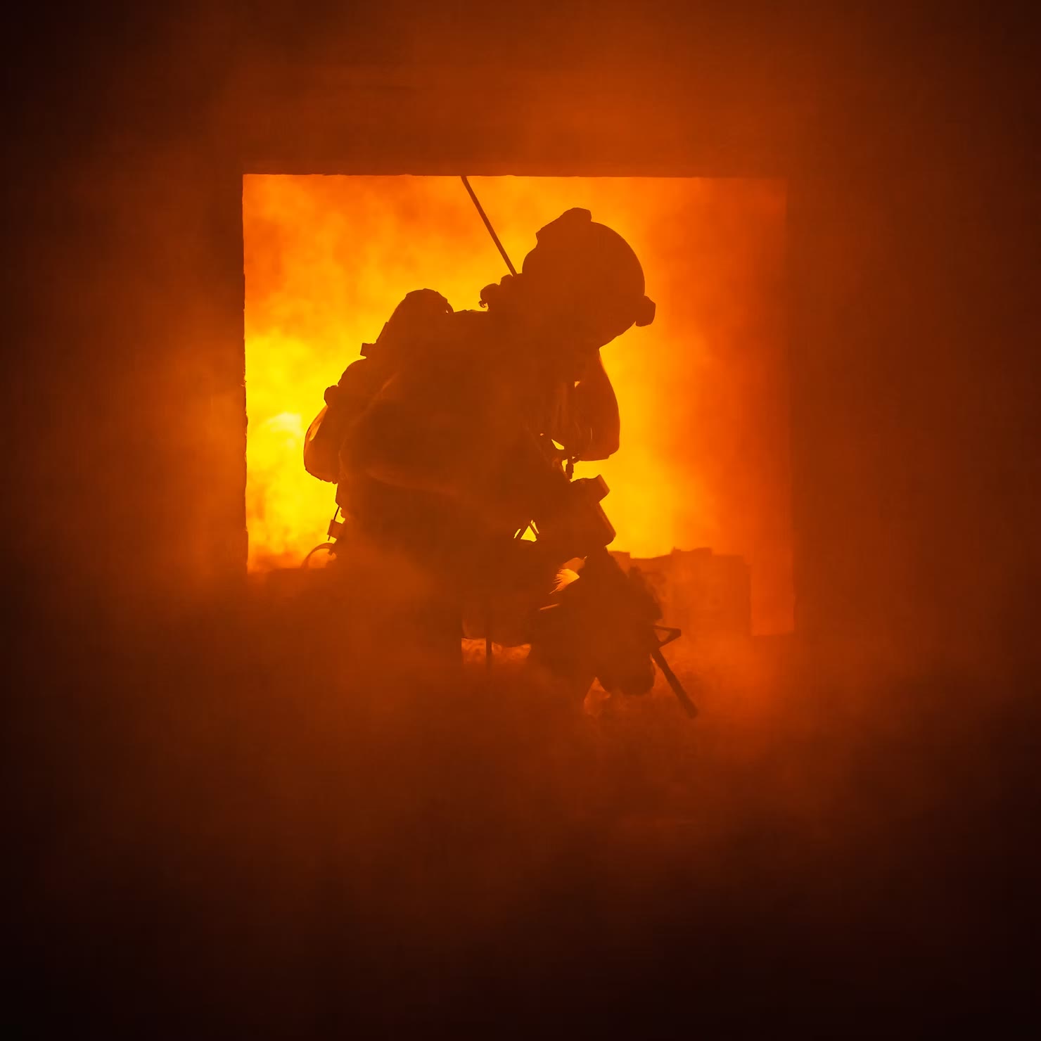 Silhouette of a firefighter in full gear crouching in front of a glowing, smoke-filled doorway
